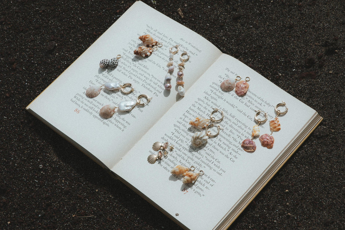 Shell earrings on an open book on dark sand