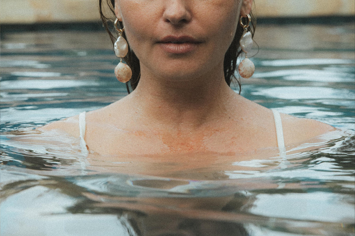Model in a pool wearing pearl and shell earrings