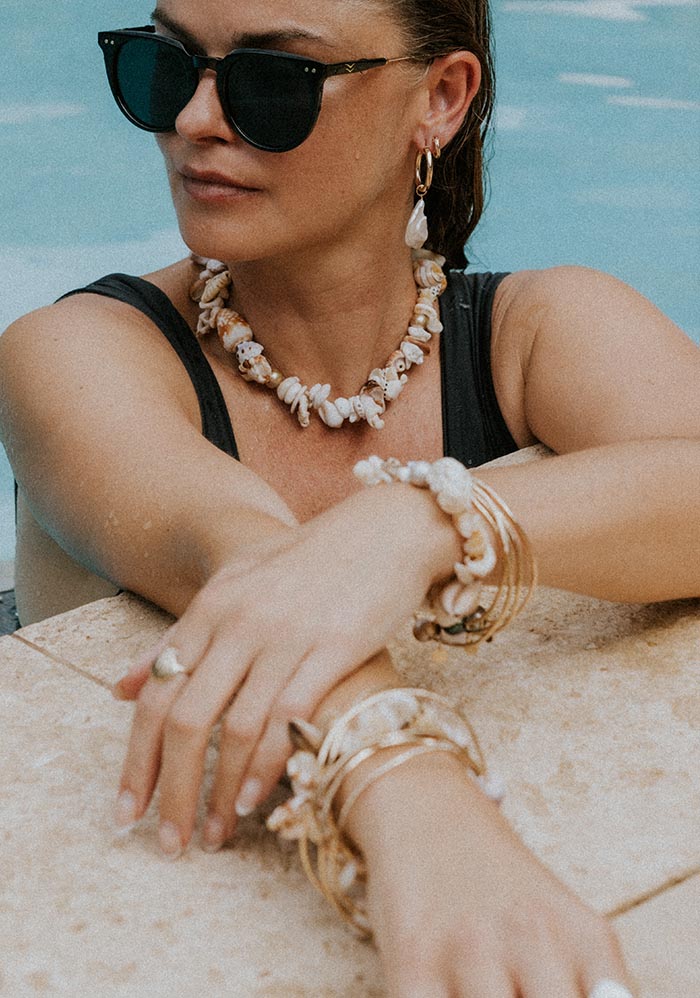 Model in sunglasses wearing shell necklaces at the pool