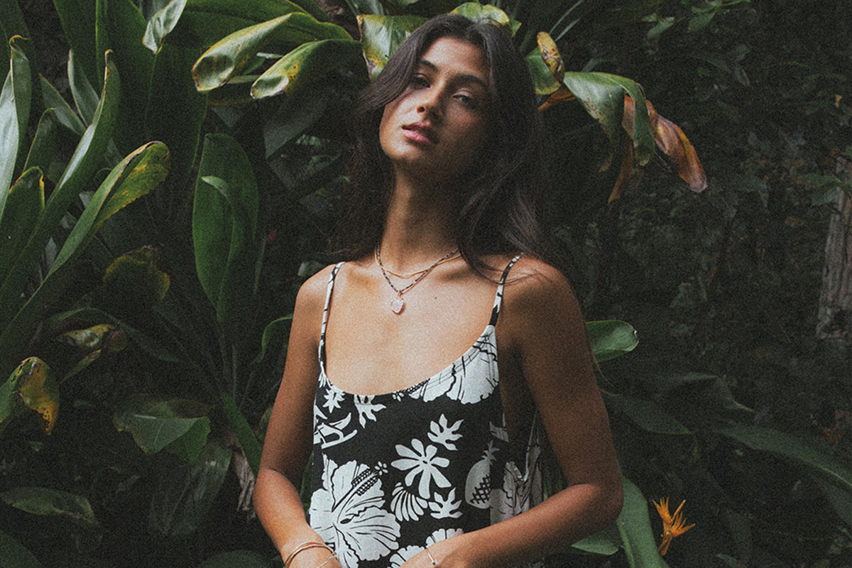 Model in a black and white tropical print dress among dark leaves