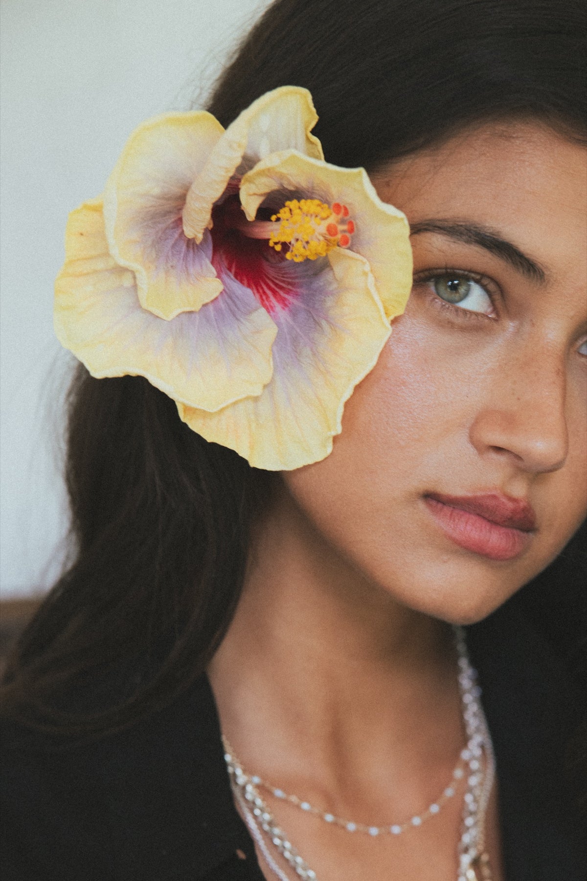 Model with a hibiscus in her hair wearing layered Wings necklaces
