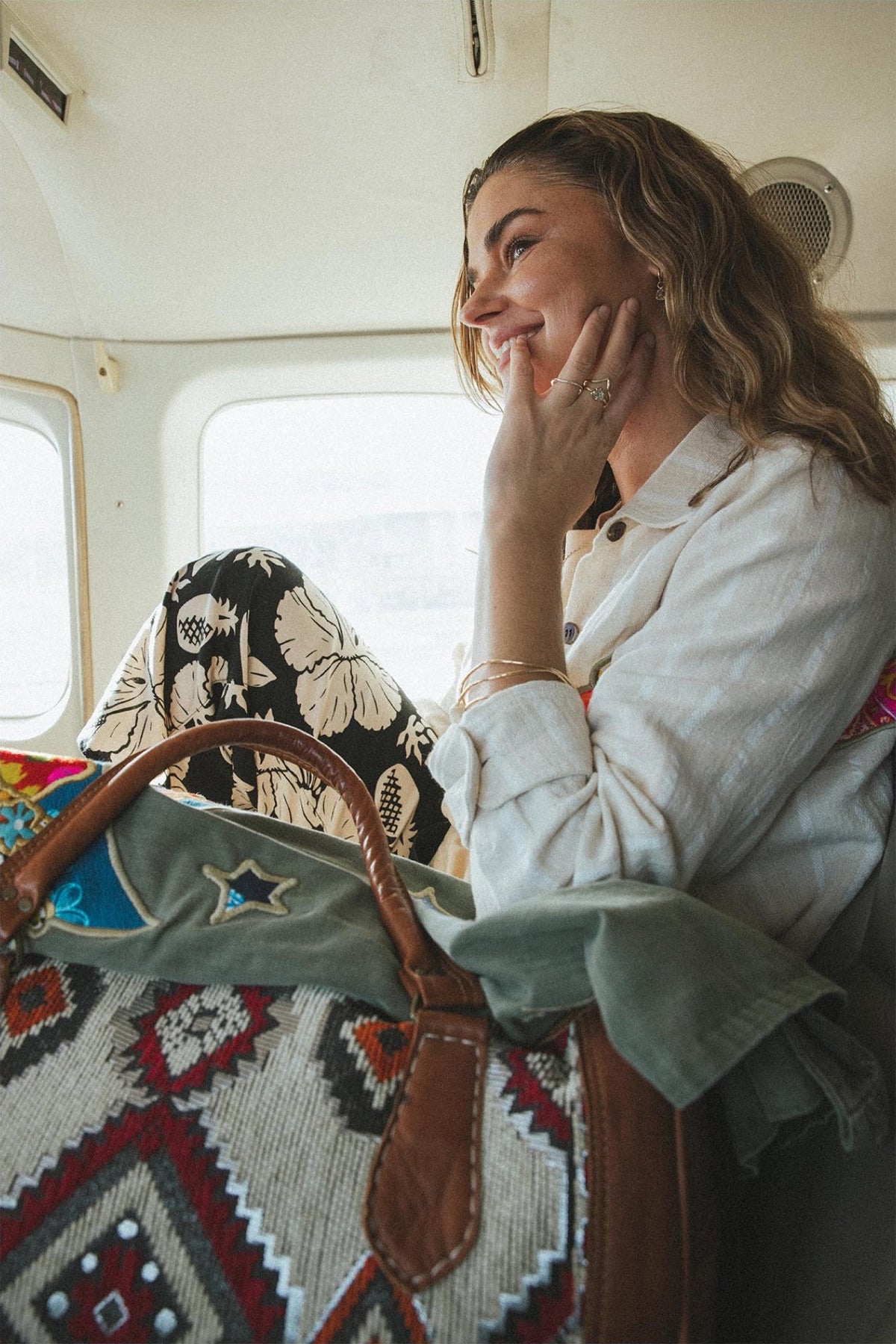 Model by a plane window with a kilim bag
