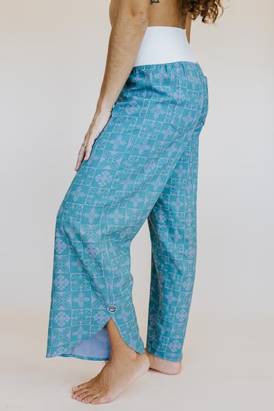 Model wearing Wings Hawaii pau hana pants in quilted ulu and plumeria print in surf blue - side view