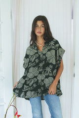 Wings Hawaii Short Sleeve Pocket Blouse in green Hana Forest aloha print. Designed in Maui, sewn in Bali. Modern women's aloha shirt. Small batch, sustainable apparel for beachy boho surfer style. Light and dark green print with hibiscus flowers, pineapples and Hawaiian outrigger canoes. 