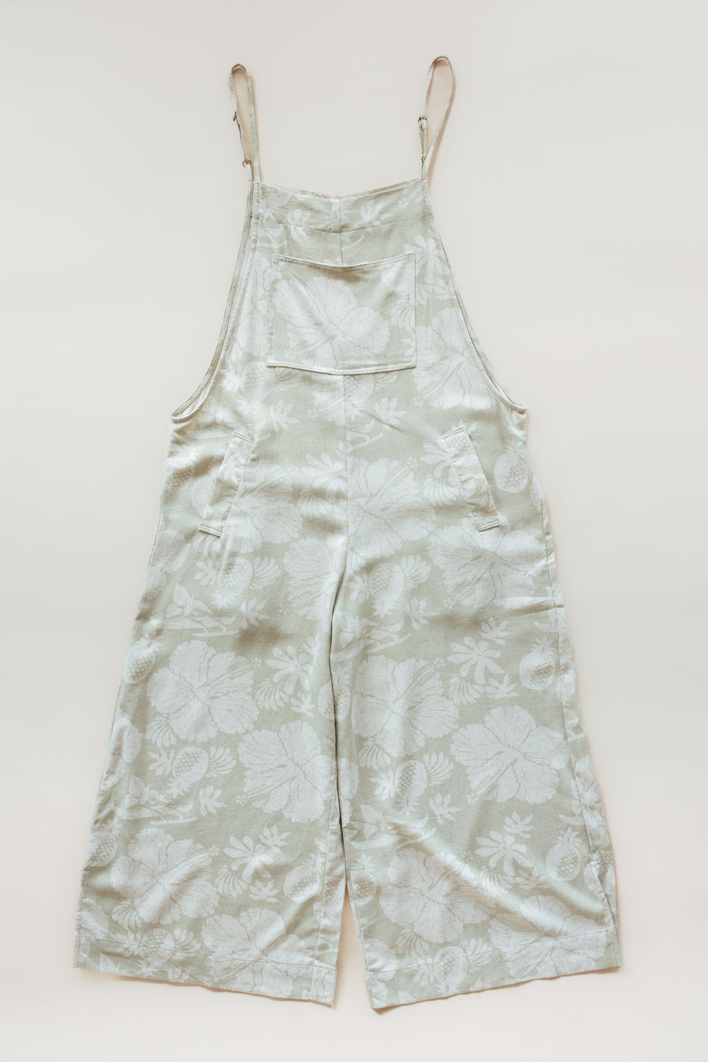 Wings Hawaii women's aloha print overalls in Hana Pearl. Designed in Maui, made in Bali. Cream white neutral tropical pattern with hibiscus florals, pineapples, and Hawaiian outrigger canoes. Adjustable straps, wide leg, relaxed fit, front and side pockets. Small batch, sustainable clothing for beachy, boho style. 