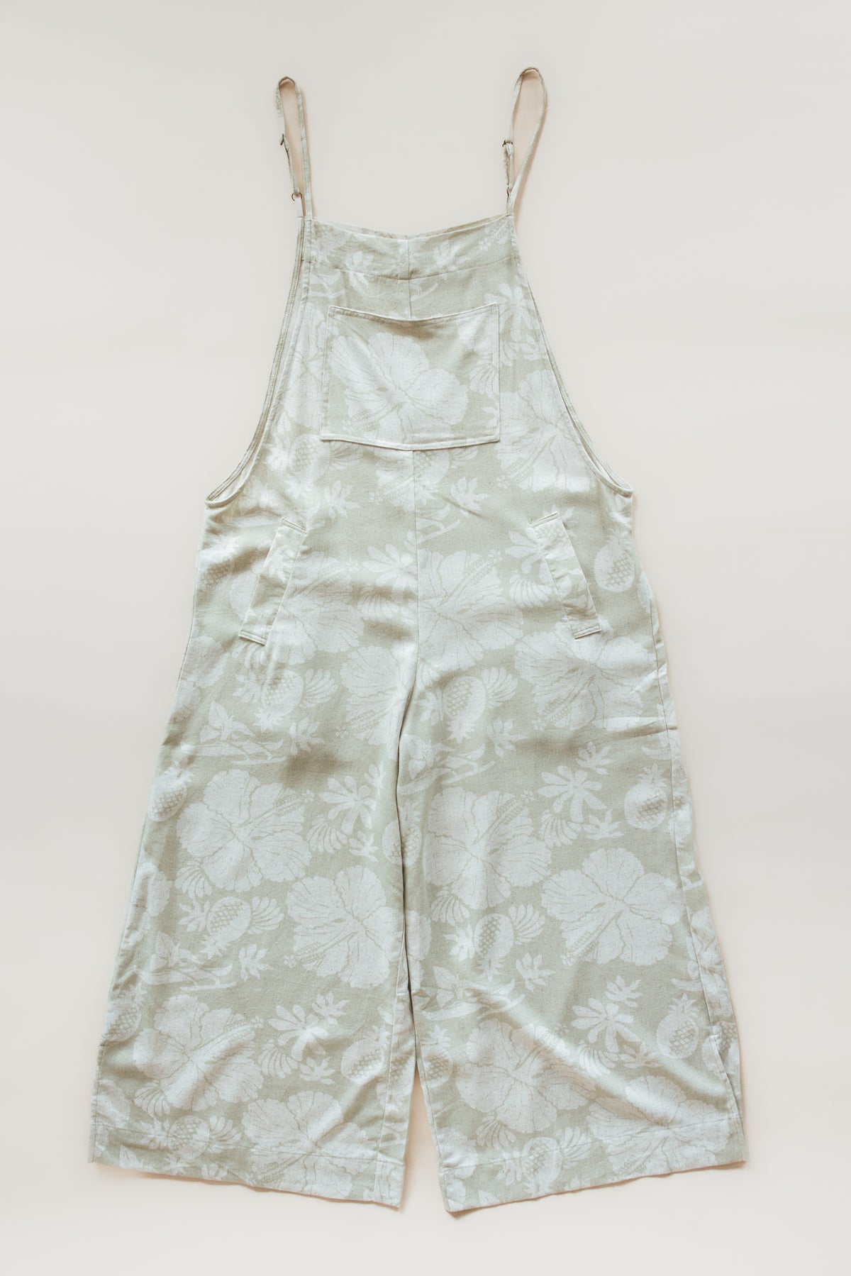 Wings Hawaii women's aloha print overalls in Hana Pearl. Designed in Maui, made in Bali. Cream white neutral tropical pattern with hibiscus florals, pineapples, and Hawaiian outrigger canoes. Adjustable straps, wide leg, relaxed fit, front and side pockets. Small batch, sustainable clothing for beachy, boho style. 
