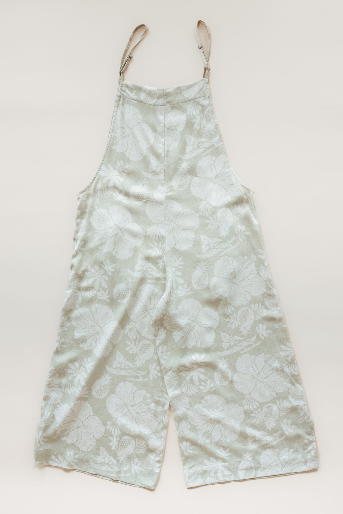 Wings Hawaii women's aloha print overalls in Hana Pearl. Designed in Maui, made in Bali. Cream white neutral tropical pattern with hibiscus florals, pineapples, and Hawaiian outrigger canoes. Adjustable straps, wide leg, relaxed fit, front and side pockets. Small batch, sustainable clothing for beachy, boho style. 
