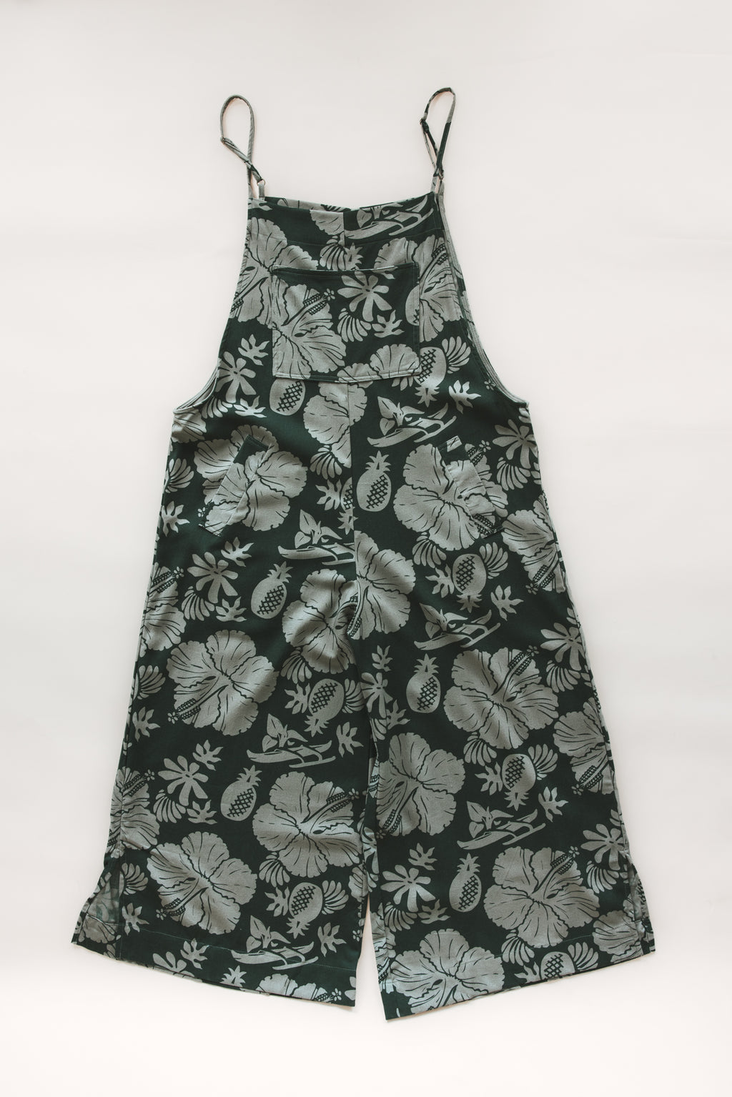 Wings Hawaii women's aloha print overalls in Hana Forest. Designed in Maui, made in Bali. Dark green tropical pattern with hibiscus florals, pineapples, and Hawaiian outrigger canoes. Adjustable straps, wide leg, relaxed fit, front and side pockets. Small batch, sustainable clothing for beachy, boho style. 