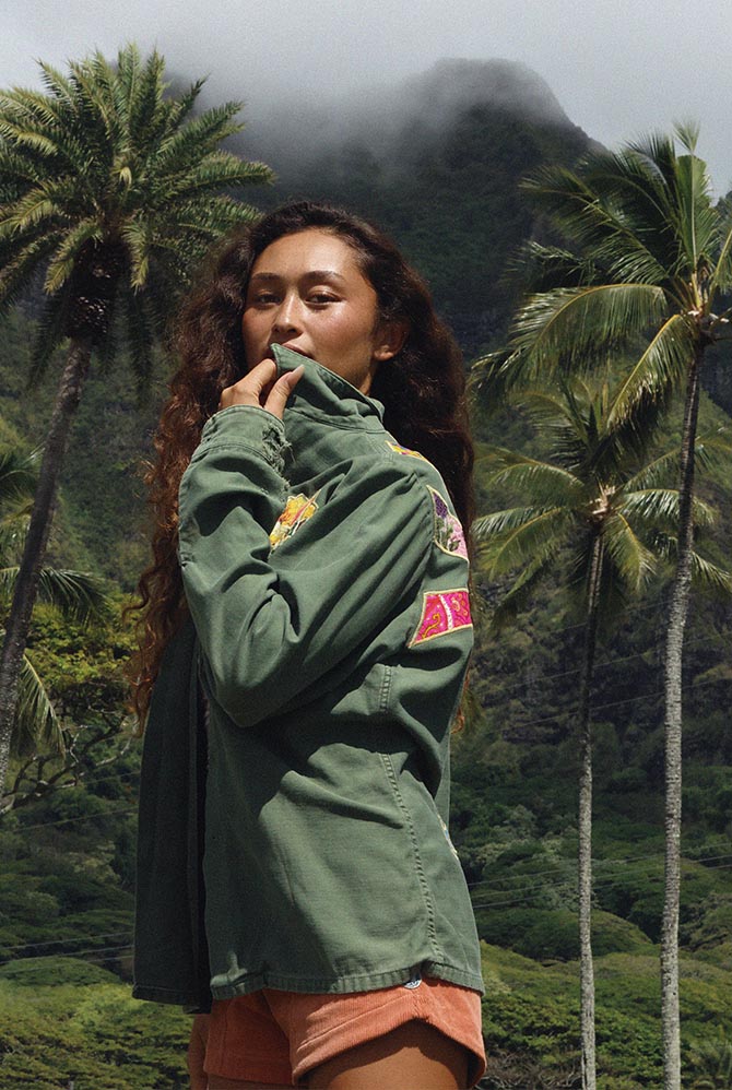 Model in an embroidered green jacket among palms