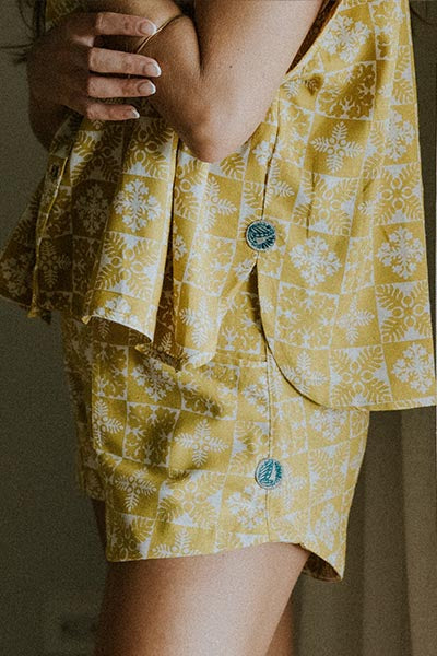 Model wearing Wings Hawaii retro pocket shorts and boxy buttun-up blouse in quilted ulu and plumeria print in marigold