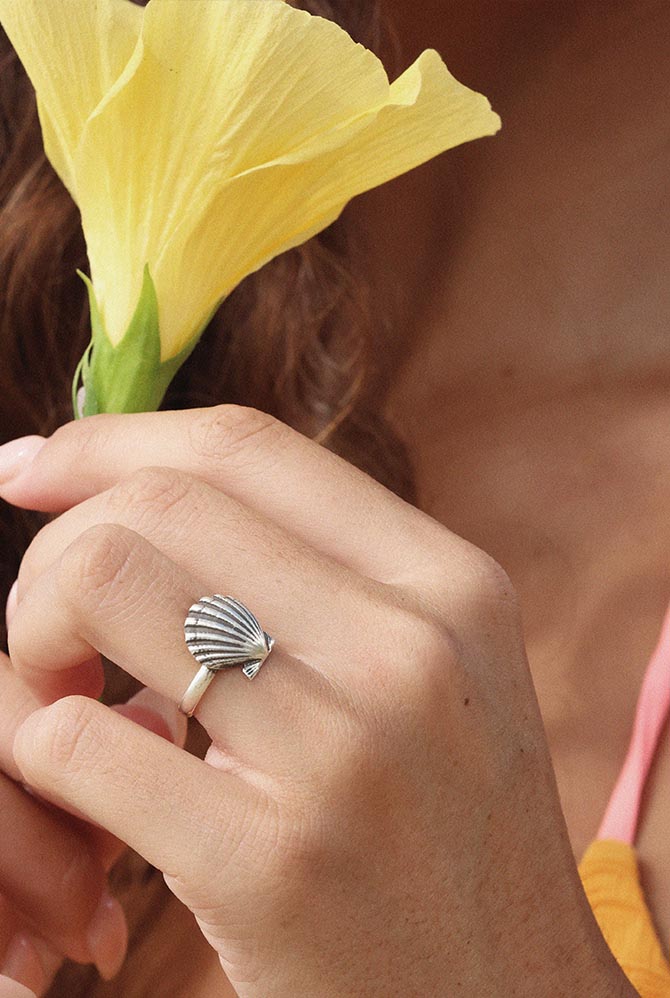 Hand with a sunrise shell ring holding a yellow flower