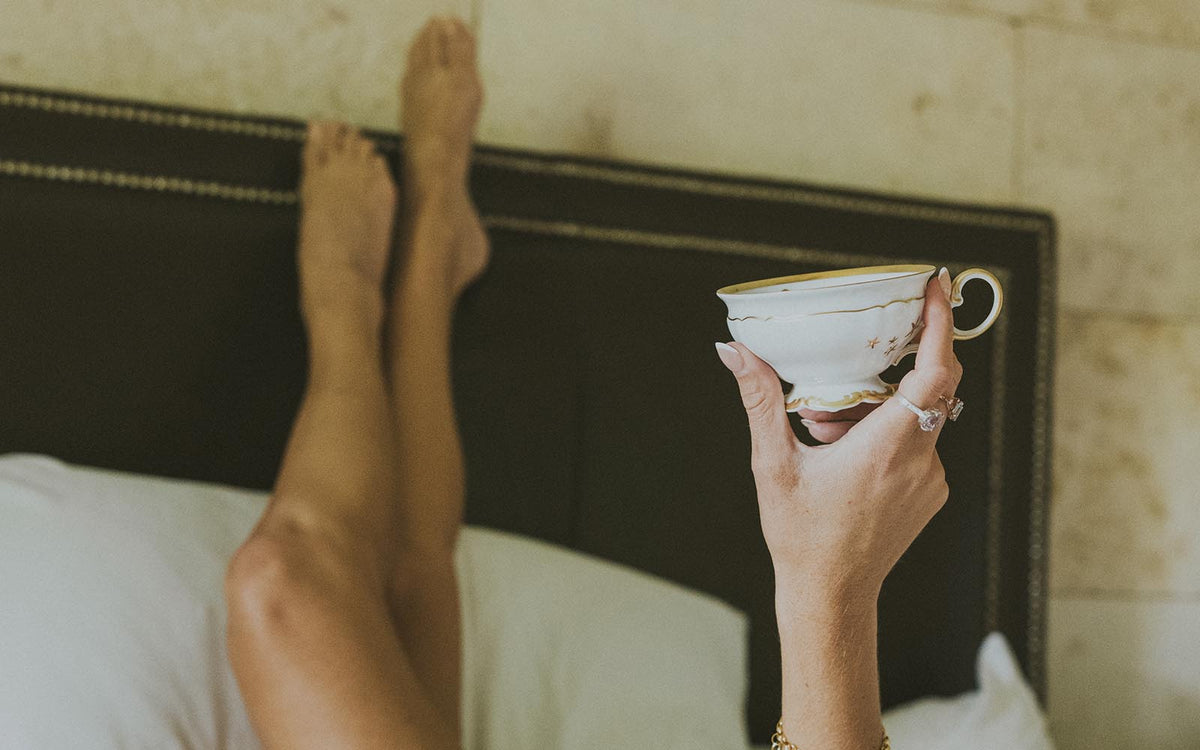 Legs crossed on a bed, holding a teacup