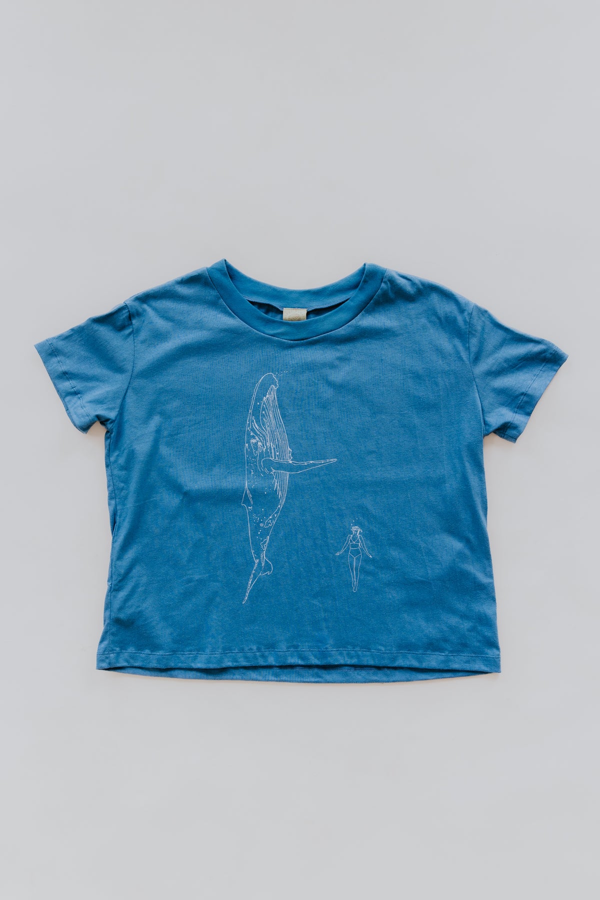 Wings Hawaii Whale Dance Crop Tee in blue. Humpback whale and diver on front, aloha design on back. Original artwork designed in Maui. Small batch, sustainable, women's apparel. 