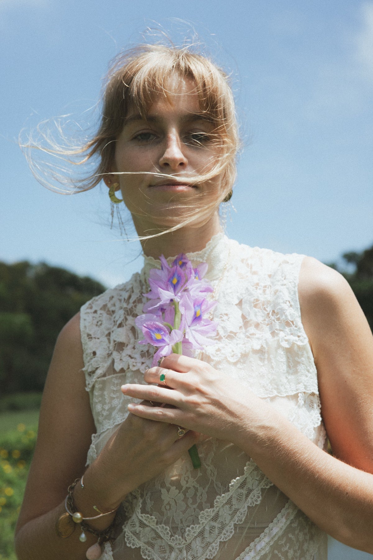 Model in a lace top holding purple blossoms against the sky, Autumn's Garden