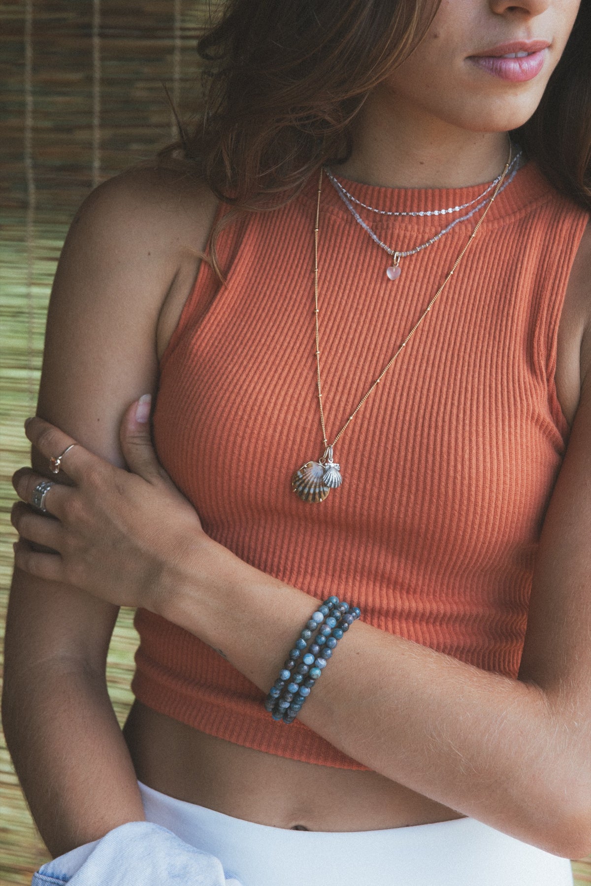 Model in a rust top wearing charm necklaces