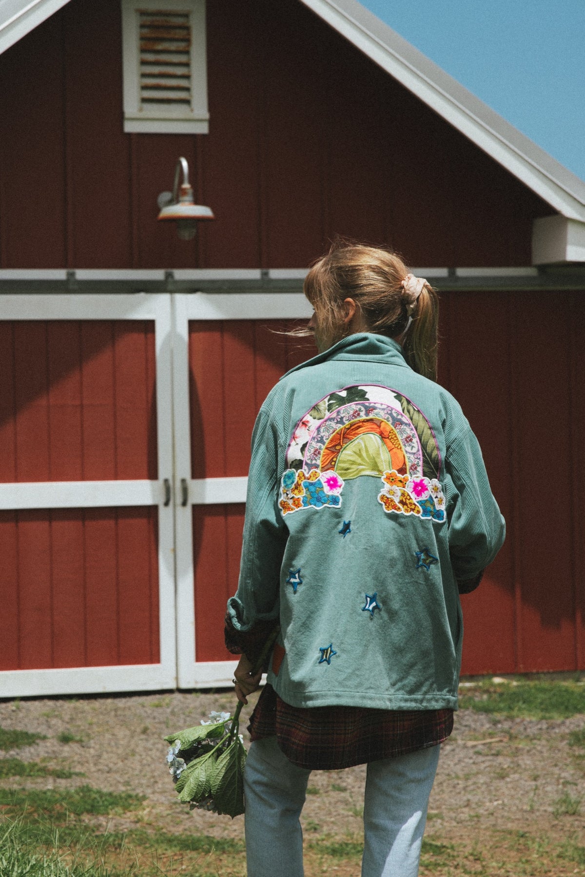 Back of a green jacket with a rainbow patch at the red barn