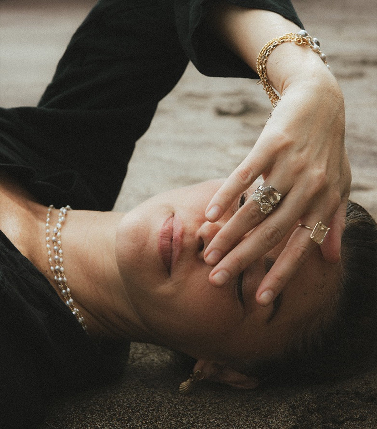 Model lying on dark sand, her hand over her face