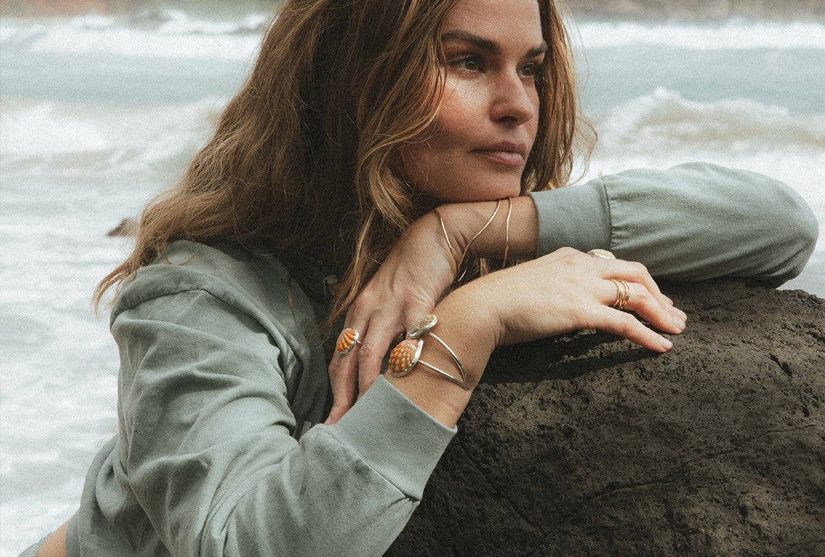 Model leaning on a rock in a sage hoodie