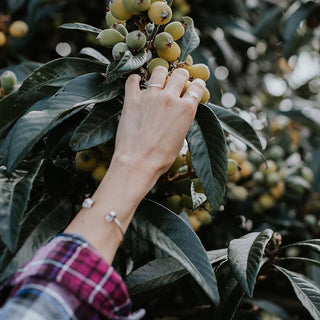 model hand wearing rings and a herkimer cuff bracelet on her arm while reaching for fruit on a tree